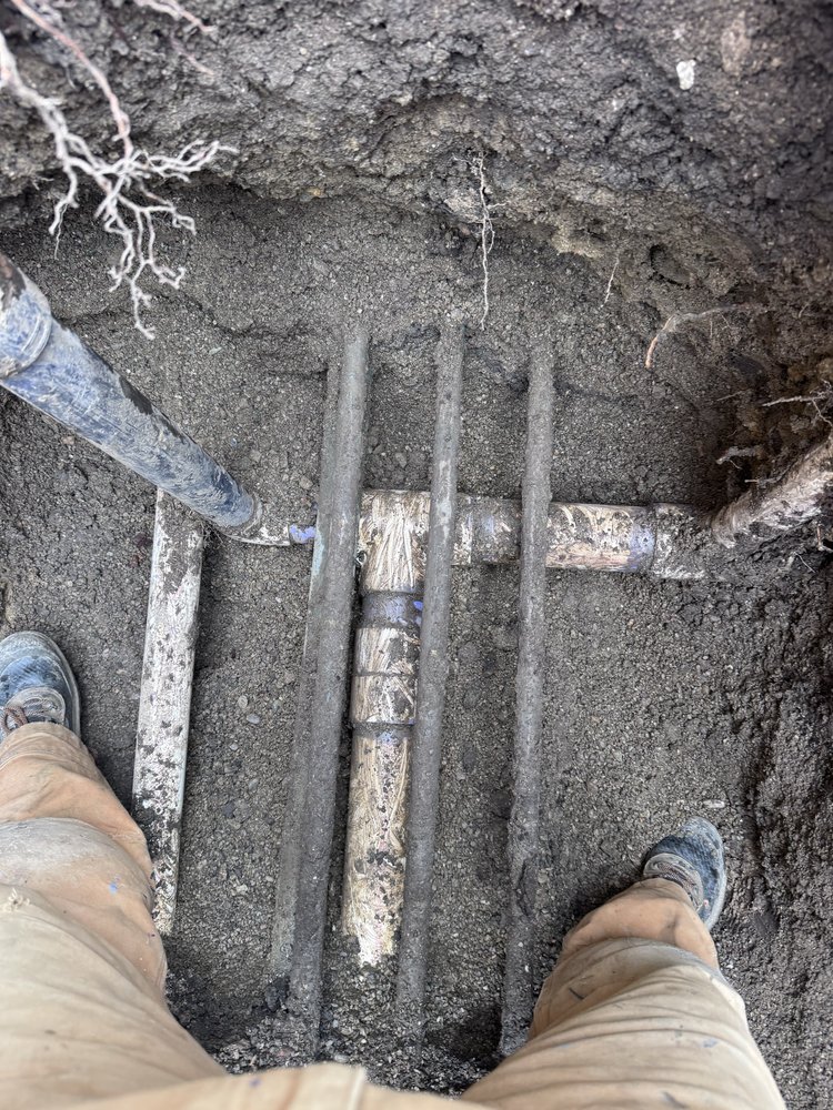 Excavated trench exposing multiple underground water and sewer lines for replacement